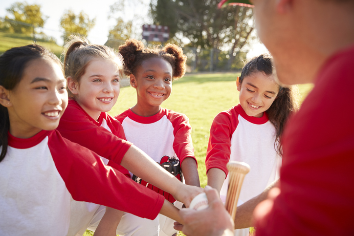 Schoolgirl baseball team in a team huddle with their coach